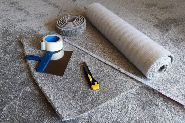 A roll of carpet with tape and scissors, symbolizing the materials used in a carpet tile flooring service in Austin, TX.
