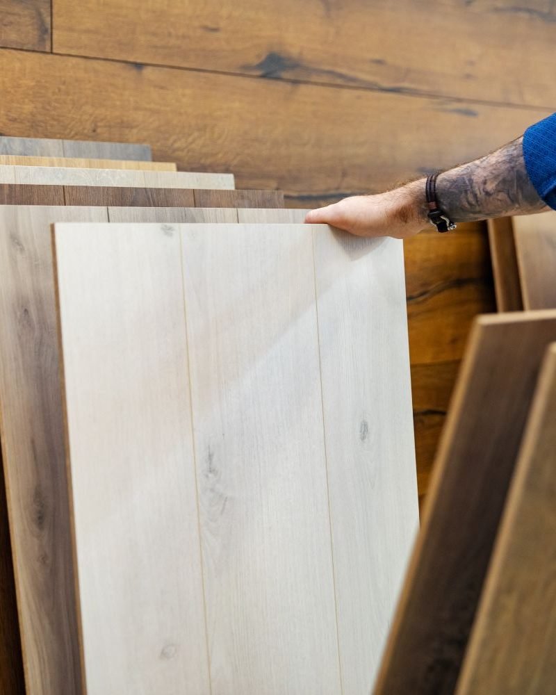 A man is holding a stack of wood flooring, highlighting a flooring service located in Austin, TX.